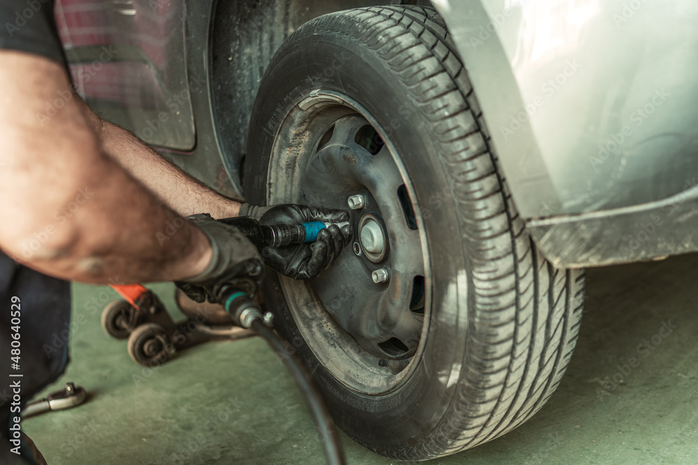 Man using an electric screwdriver to remove a wheel in a garage