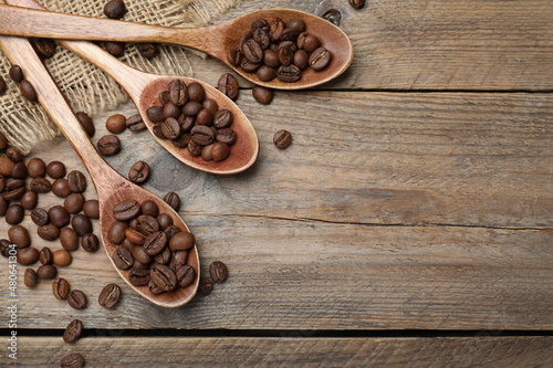Spoons with roasted coffee beans on wooden table, flat lay. Space for text