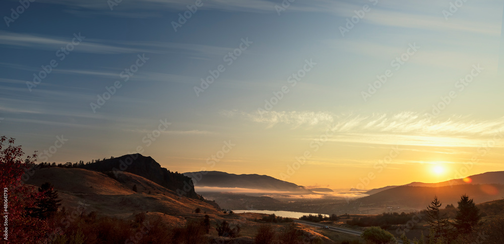 Fototapeta premium panorama of sunrise over a village located by a lake between mountains and hills