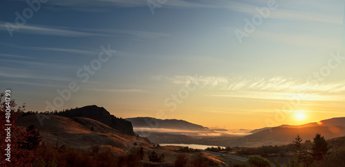 panorama of sunrise over a village located by a lake between mountains and hills