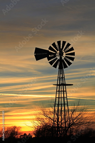 windmill silhouette at sunset with colorful clouds and trees north of Hutchinson Kansas USA that's bright and colorful out in the country. 