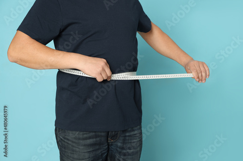 Man measuring waist with tape on light blue background, closeup