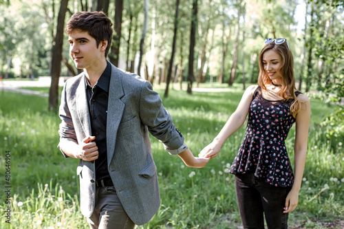 The guy leads the girl by the hand. A couple in love walks in a spring park holding hands. Young couple walking in a spring park on Valentine's Day.