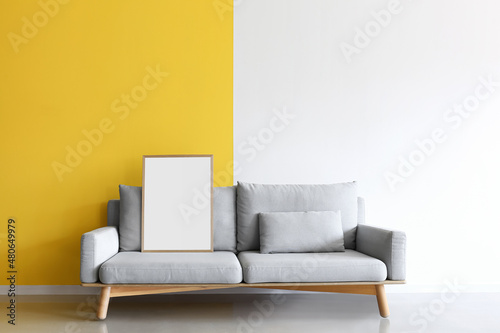 Cozy grey sofa with blank frame near yellow and white wall