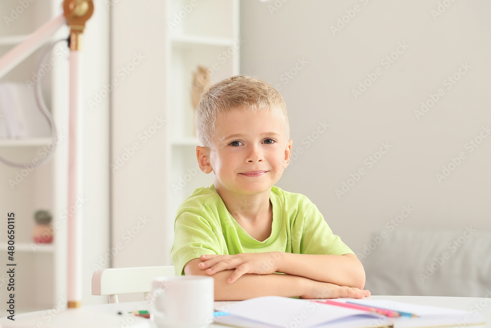 Adorable little boy sitting at table in room Adorable little boy sitting at table in room