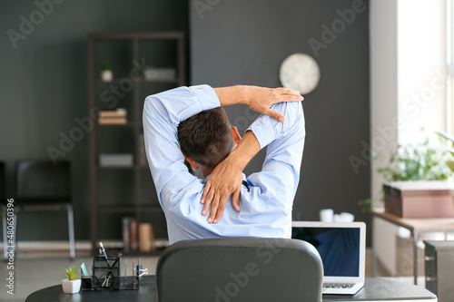Fotografie Young businessman stretching his spine while working in office