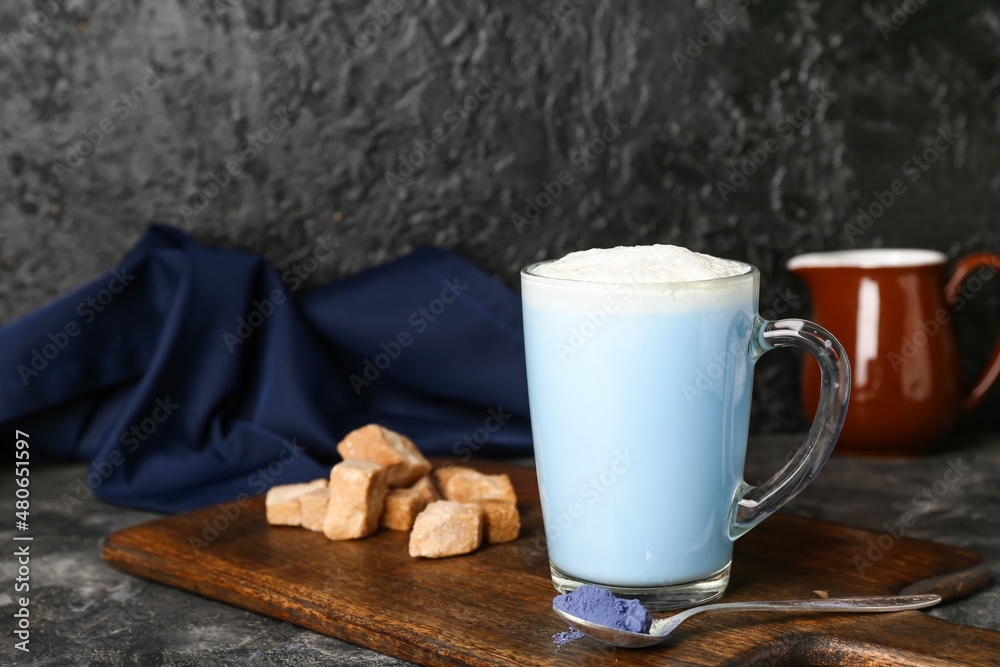 Wooden board with cup of blue matcha latte, powder and sugar on dark background Wooden board with cup of blue matcha latte, powder and sugar on dark background
