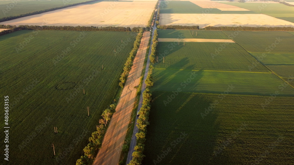 Drone flying over road between different agricultural fields during dawn sunset.
