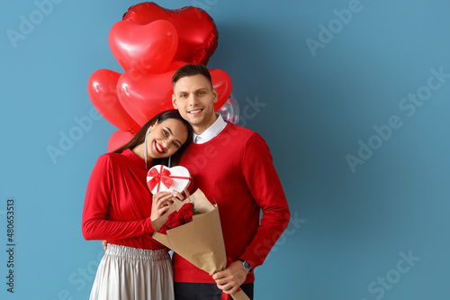 Happy young couple with gift, flowers and balloons on color background. Valentine's Day celebration