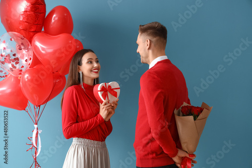 Young man greeting his girlfriend for Valentine's Day on color background