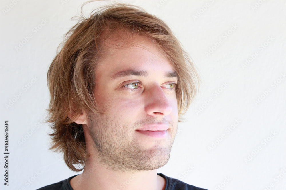 Obraz premium Young man with green eyes smiling candid. Young man with long blonde hair smiling candidly isolated on white background. Facial expressions of a young guy. Men with positive smile portrait of a person