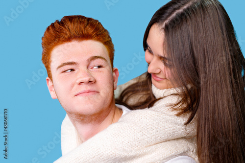 Close up photo of a red hair boyfriend and his brunette girlfriend looking at each other, he holds her on the back and smiling.