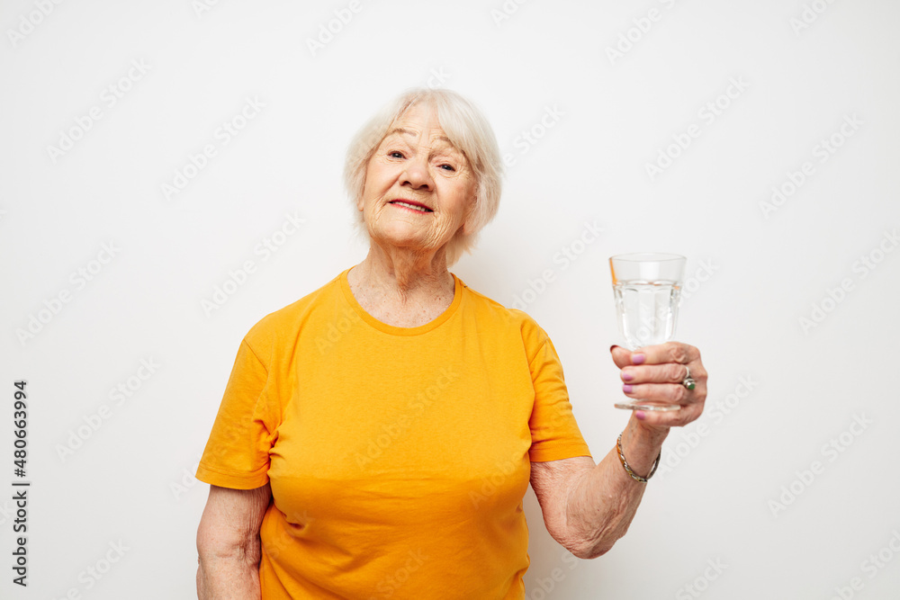 smiling elderly woman in yellow t-shirts a glass of water in his hands cropped view smiling elderly woman in yellow t-shirts a glass of water in his hands cropped view