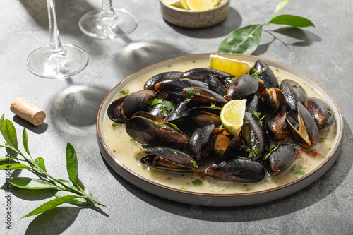 Black mussels in garlic sauce with herbs and lime and two glasses of white wine on the table under the summer sun