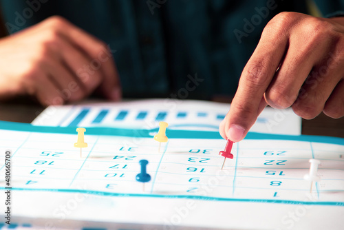 Hand pin on business desk calendar with office equipment concept of event planner or personal organization reminder and schedule or planning.