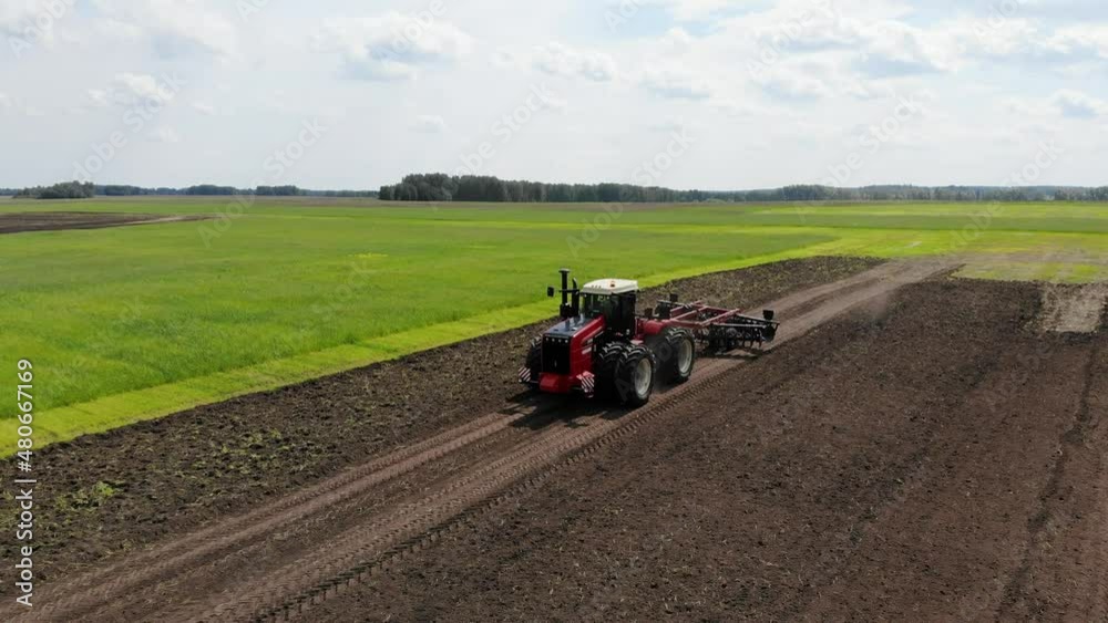 Red harvester drives across field and plows earth. Sows grain in field. He drives and leaves tracks in form of stripes. Russian field, harvesting, grain, agriculture, cultivation, modern technologies Red harvester drives across field and plows earth. Sows grain in field. He drives and leaves tracks in form of stripes. Russian field, harvesting, grain, agriculture, cultivation, modern technologies