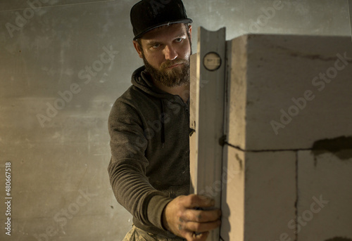 a male  builder puts a wall of aerated concrete in his house, in his hand  a level, he put it against the wall. © Olga
