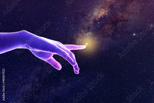 Hand of God universe creation concept. A sparkling star covered purple and pink lit hand points to a small ball of light in the Milky Way.