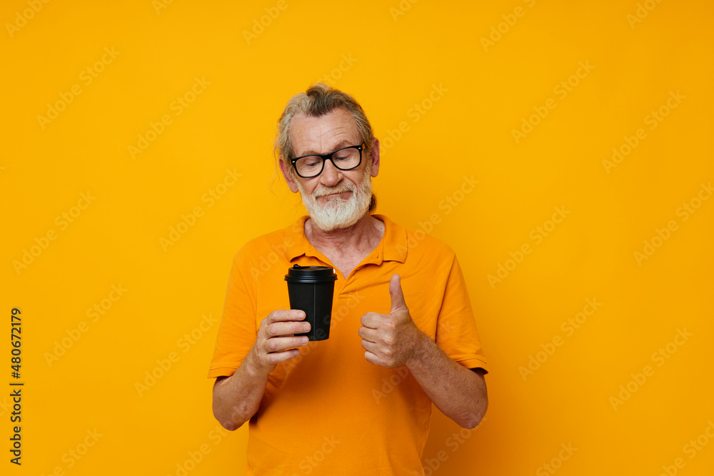 Senior grey-haired man in a yellow T-shirt a glass with a drink unaltered Senior grey-haired man in a yellow T-shirt a glass with a drink unaltered