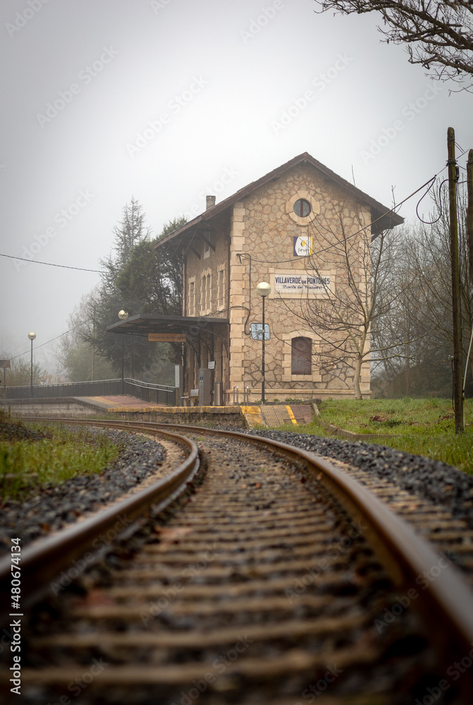 Fototapeta premium Villaverde de Pontones, Spain. December - 16 - 2021. A train track leads us to gaze at the Villaverde de Pontones Train Station on a foggy day
