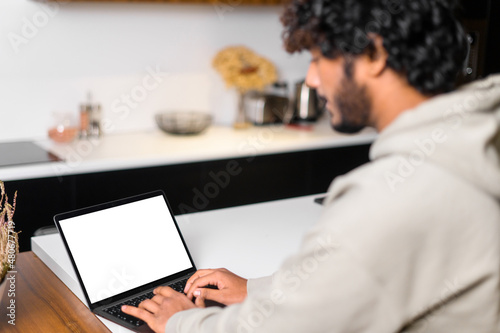 Video call concept. Indian man is using laptop with blank empty screen, making video call, using new computer app for video connection, back view, copy space, template