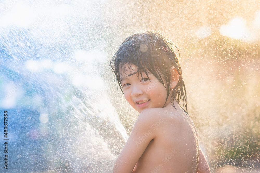 Obraz premium asian boy has fun playing in water from a hose outdoors