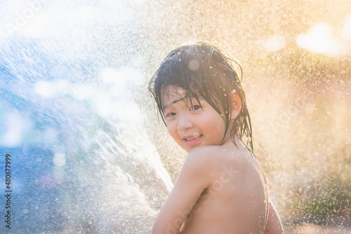 asian boy has fun playing in water from a hose outdoors