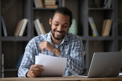 Happy cheerful African student guy reading admission letter from school, university, college, receiving paper document, smiling, laughing. Millennial businessman getting good deal, contract