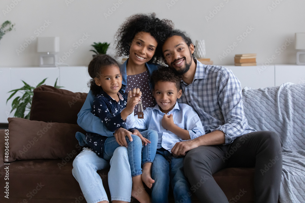 Happy young African parents and two sweet little kids holding keys from new apartment. Family of home owners, tenants, renters sitting on sofa, enjoying being at home. Head shot portrait Happy young African parents and two sweet little kids holding keys from new apartment. Family of home owners, tenants, renters sitting on sofa, enjoying being at home. Head shot portrait