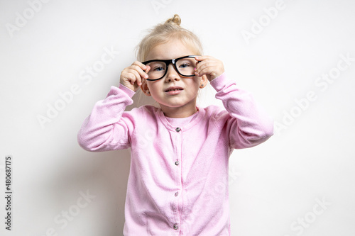 Beautiful child girl in glasses in a pink sweater on a light background.