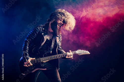 Emotional portrait of a rock guitar player with long hair and beard plays on the smoke background