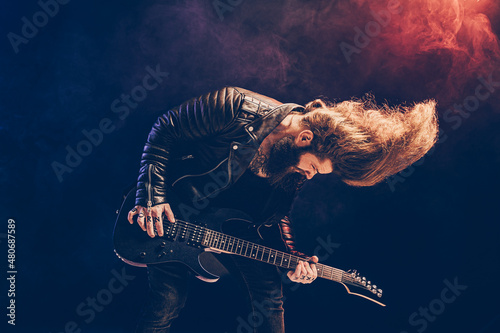 Fotografie Emotional portrait of a rock guitar player with long hair and beard plays on the