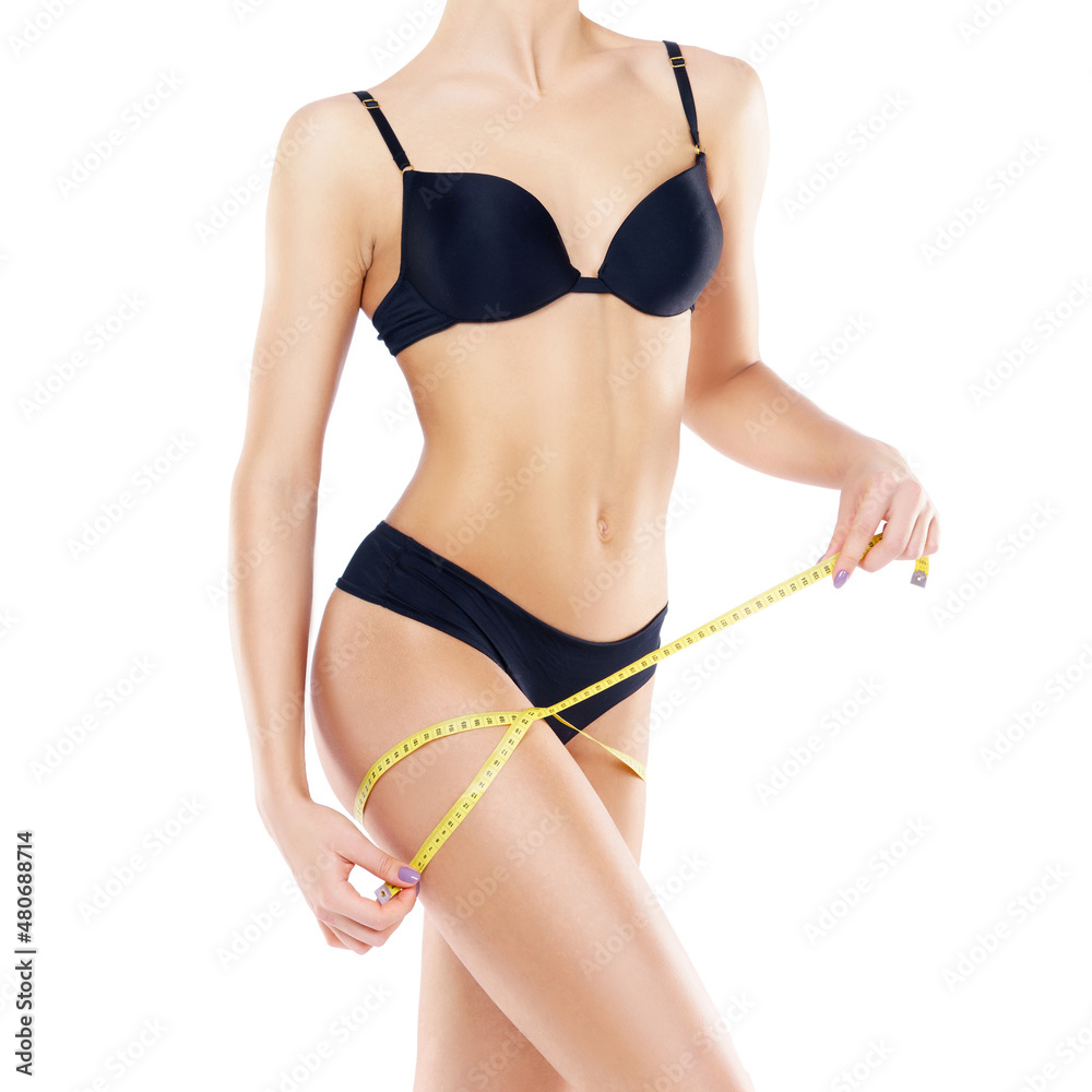 Fototapeta premium Young and fit female body close-up. Waist of beautiful and slender woman with measuring tape isolated on white. Sport, fitness, diet and healthy eating concepts.