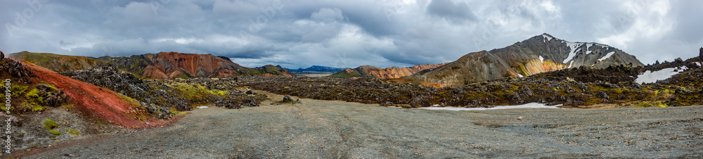 Fototapeta premium Beautiful panoramic Icelandic landscape of colorful rainbow volcanic Landmannalaugar mountains, at famous Laugavegur hiking trail with dramatic snowy sky, and red volcano soil in Iceland.