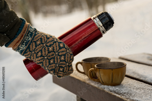 Picnic for two. A red thermos with tea and two mugs outside. Ragged wool gloves.