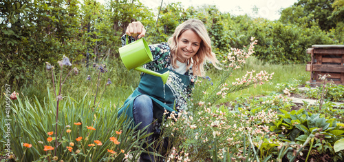 pretty blonde gardener working in garden with flowers and wearing green work apron