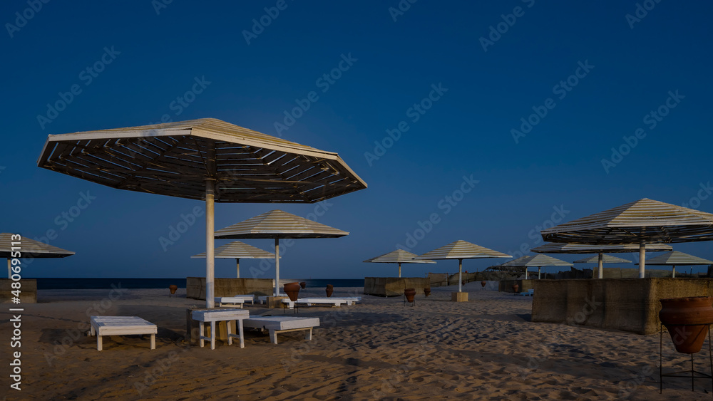 Overnight on the Red Sea beach. Lattice sun umbrellas on the background of a deep blue sky. Empty sun beds and clay urns on the sand. There is no one. Egypt