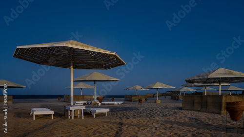 Overnight on the Red Sea beach. Lattice sun umbrellas on the background of a deep blue sky. Empty sun beds and clay urns on the sand. There is no one. Egypt