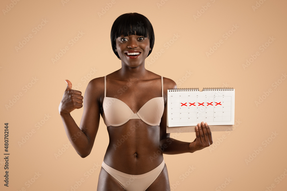 Fototapeta premium CHeerful black woman in underwear with calendar showing thumb up