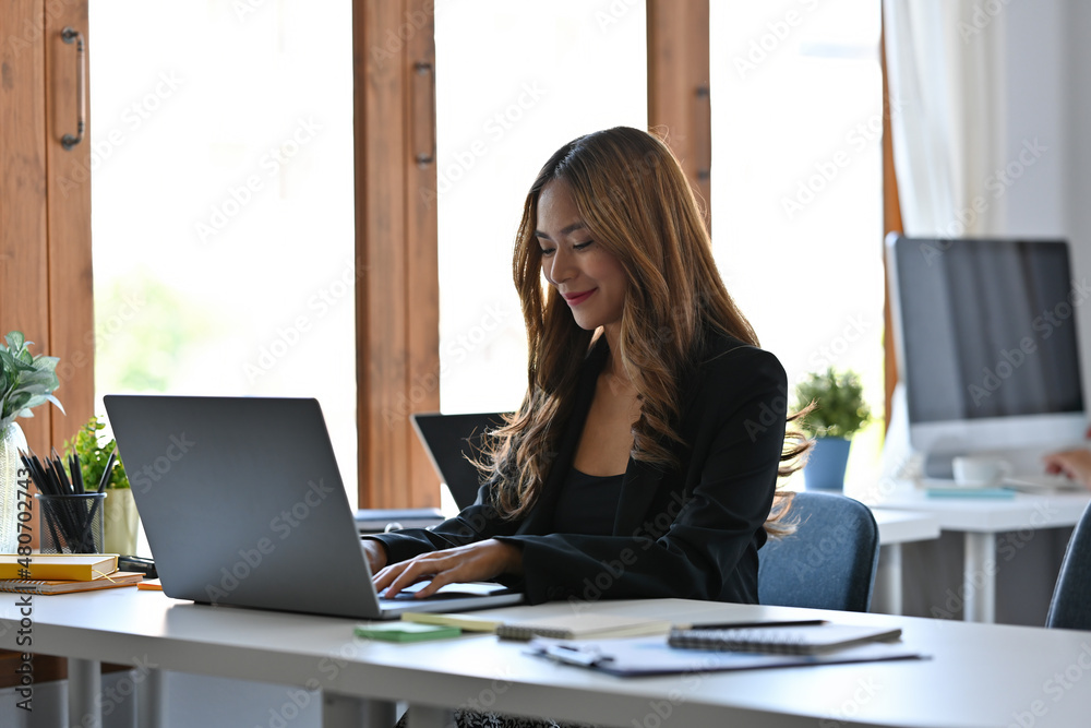 Photo of a young businesswoman sitting at the white working desk surrounded by a computer laptop and various office stuff. Photo of a young businesswoman sitting at the white working desk surrounded by a computer laptop and various office stuff.