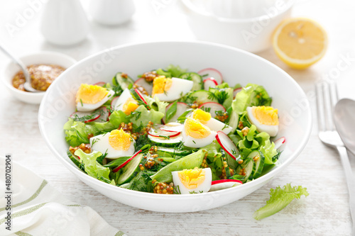 Easter fresh vegetable salad with boiled egg, radish and cucumber, dressing with dijon mustard and lemon on white wooden table