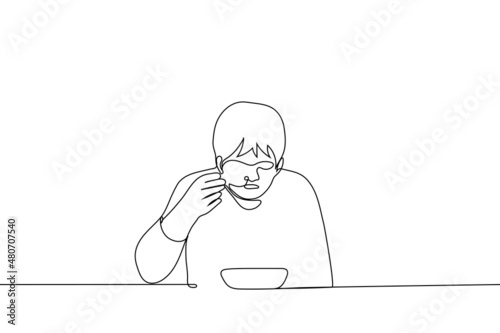 man sits at table and eats soup from deep bowl bringing spoon to his mouth - one line drawing vector. concept of eating hot broth, soup; sick person eats broth