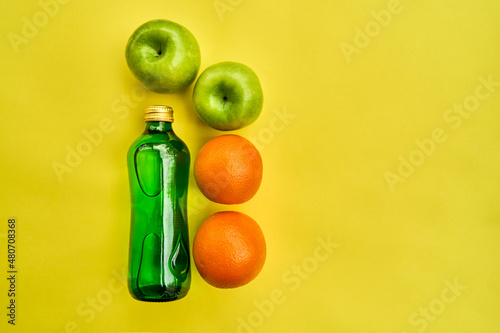 green bottle, apples, oranges on a yellow background. place for text. healthy eating.healthy lifestyle