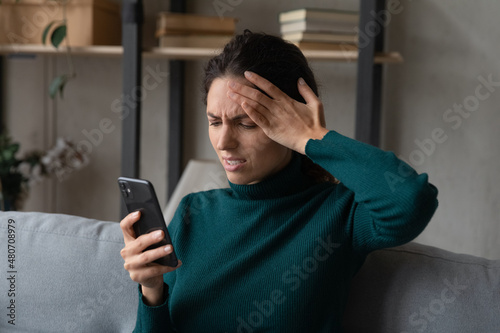 Stressed unhappy young woman checking social networks looking at telephone screen, feeling confused getting message or email with bad news, dissatisfied with broken device or wrong application work.