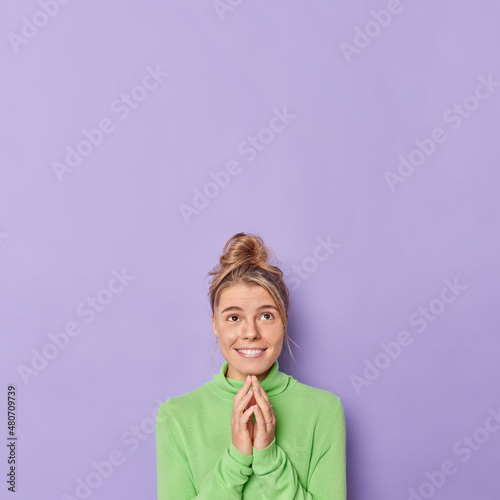 Photo Vertical shot of hopeful cheerful woman keeps hands together looks above smiles