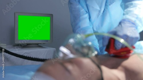 Doctor in operating room trying to help on intensive care patient, use defibrillator electrical device to shock heart. Looks at the monitor with vital data. Green Screen