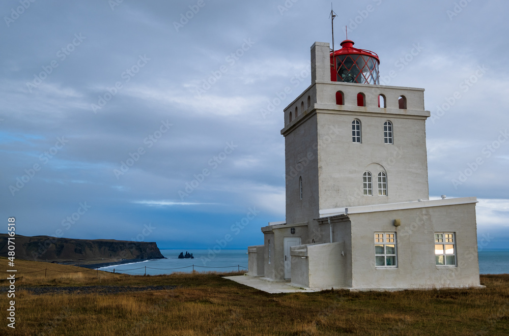 Picturesque autumn evening view to Dyrholaey lighthouse and Reynisfjara ocean  black volcanic sand beach in far, Vik, Iceland. The present lighthouse was built in 1927.