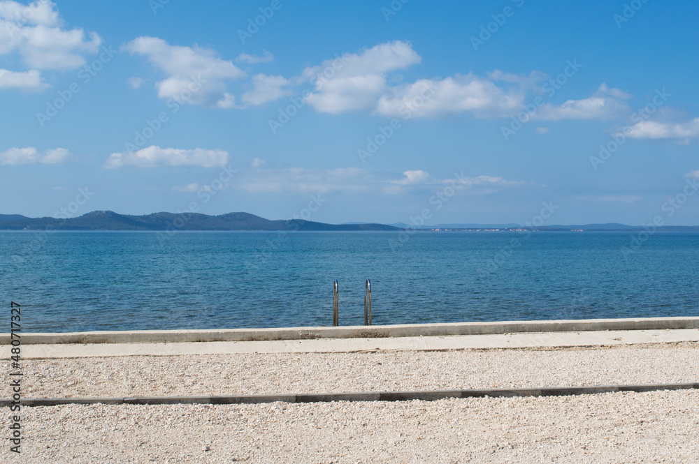 Fototapeta premium Quit and empty beach and blue sea, relaxing vacation concept with blue Adriatic sea and beach overlooking the opposite islands in Zadar, Croatia