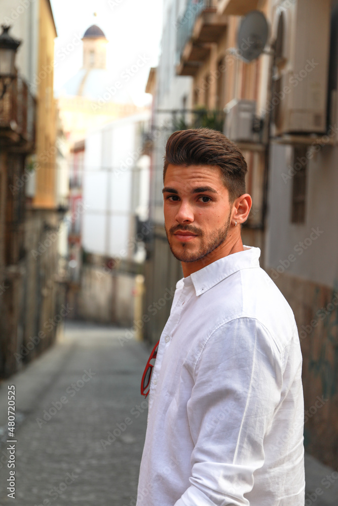 handsome dark-haired guy with a beard posing as a model in the city of Alicante with white shirt