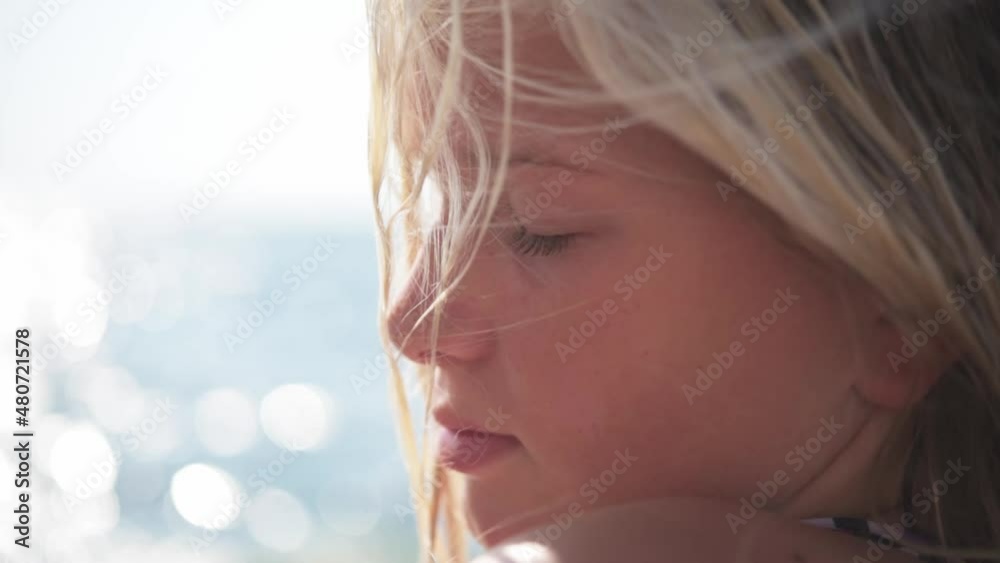 A young blond girl at seaside with her hair blown by wind